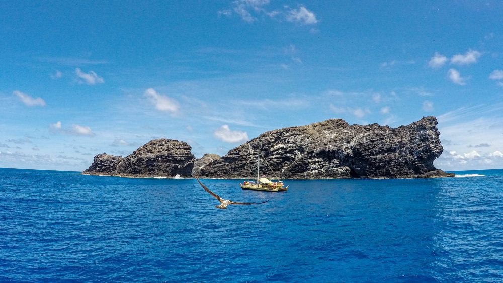 a traditional sailing vessel in beautiful blue water alongside a rocky outcropping